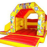 A bouncy castle with a slide on the left side. Red and yellow with a party theme.